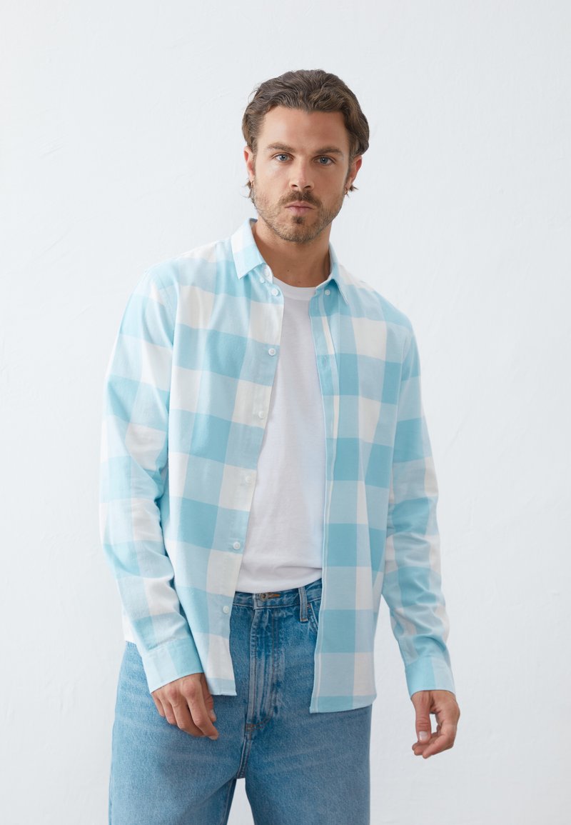 Hellblau-weiß kariertes Hemd mit Knöpfen, langen Ärmeln, über einem weißen T-Shirt getragen, kombiniert mit hellblauen Jeans. Glatte Textur.