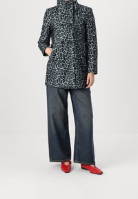 Cappotto con stampa leopardata in colori scuri, dotato di colletto alto e chiusura doppiopetto. Abbinato a pantaloni in denim a gamba larga e scarpe rosse.