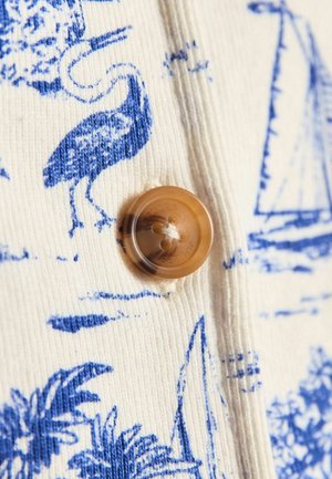 Materiał z guzikami o kremowym tle, na którym znajduje się niebieski wzór ptaków i żaglówek, uzupełniony okrągłym brązowym guzikiem.