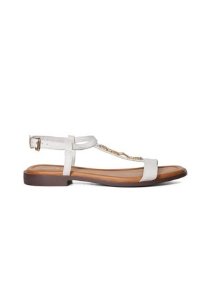 Sandales plates blanches avec un design T-bar, des sangles texturées, des accents en métal doré et une semelle marron. Bride de cheville réglable pour un ajustement optimal.