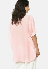 Camicia sovradimensionata a quadri rosa con maniche corte arrotolate, colletto a punta e tasca sul retro. Tessuto leggero, vestibilità comoda.