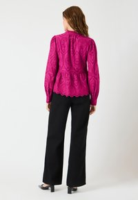 Fuksiaøyet bluse med lange ermer, peplum liv og bølget kant. Kombinert med svarte bukser og sko med blokkhæl.