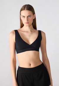 Bralette nera con design a V profonda, spalline larghe e finitura senza cuciture. Realizzata in un morbido tessuto elasticizzato per il massimo comfort.