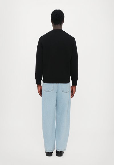 Sweat-shirt noir avec un col arrondi, associé à un jean bleu clair ample. Présente un design simple et des lignes épurées.
