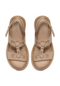 Sandali in pelle beige con suola piatta, dotati di due cinturini regolabili, dettagli in metallo dorato e anelli decorativi circolari.