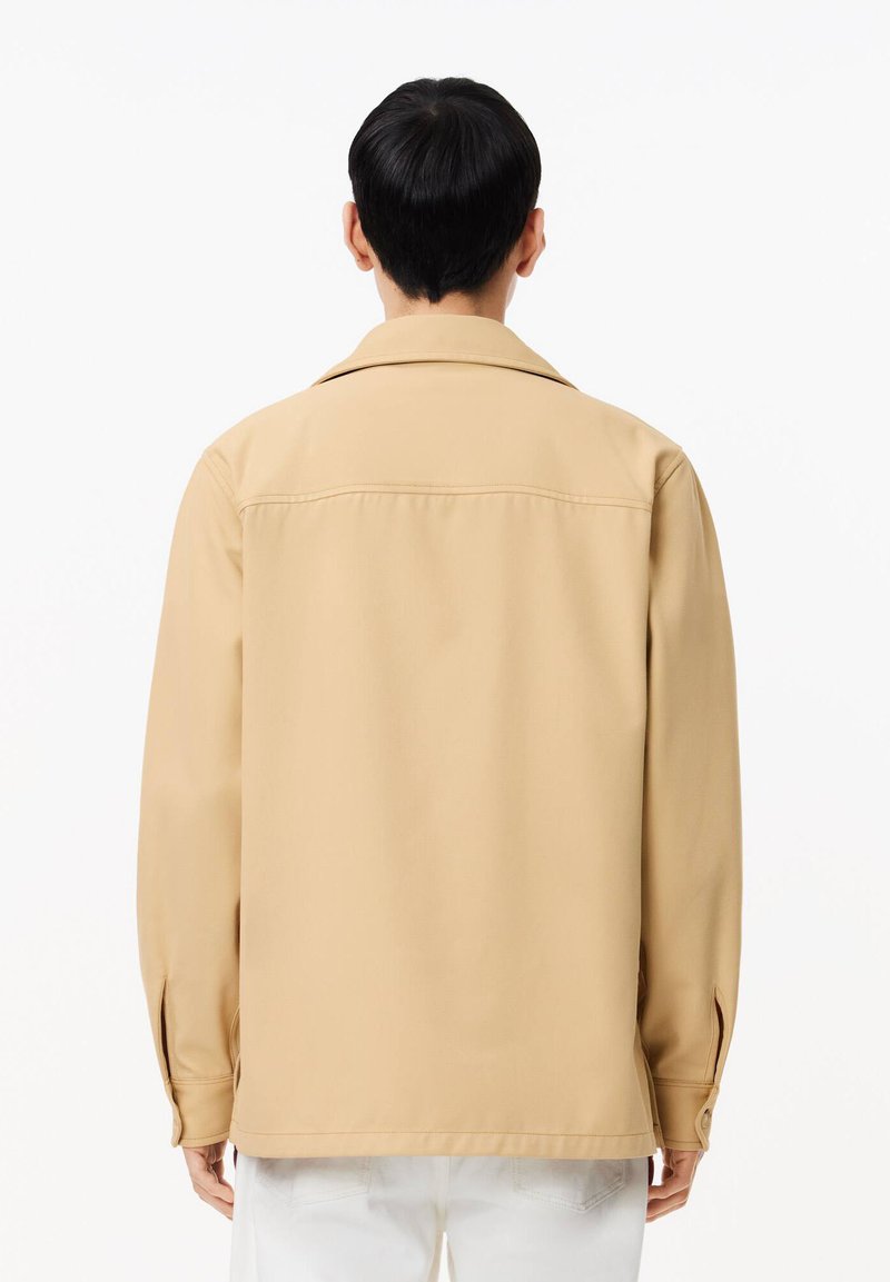 Beige Jacke mit glatter Textur, Kragen-Design und langen Ärmeln. Verfügt über einen geraden Schnitt und Knopfdetails an den Manschetten.
