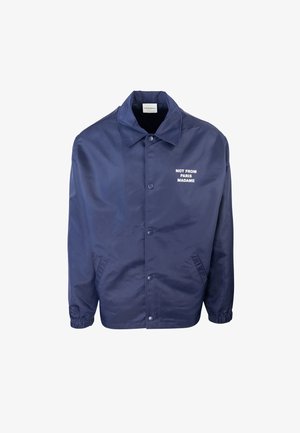 Giacca leggera blu navy in tessuto morbido, con colletto, bottoni a pressione e testo bianco "NON DA PARIGI MADAME" sul petto.
