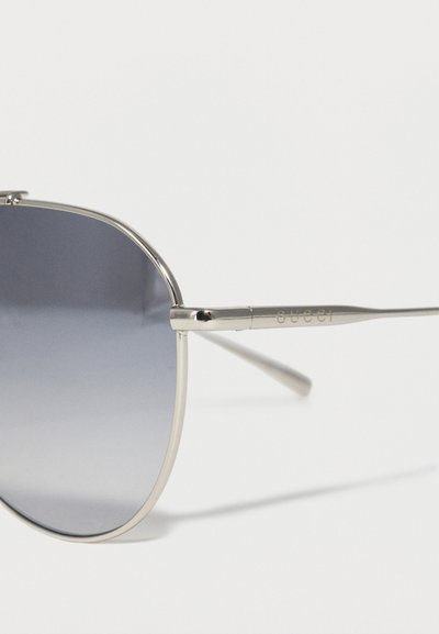 Γυαλιά ηλίου με ασημένιο μεταλλικό σκελετό και γκρι φακούς με διαβάθμιση, με το «Gucci» χαραγμένο στον λεπτό βραχίονα του σκελετού.