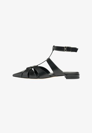 Sandale plate en cuir noir avec bout pointu, brides tressées sur le pied, bride à la cheville avec boucle argentée et petit talon.