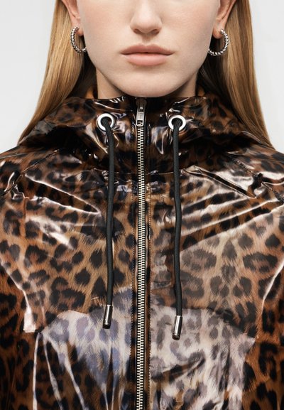 Κοντινό πλάνο ενός ατόμου που φορά σκουλαρίκια σε σχήμα κρίκου και λαμπερό ζακέτα με φερμουάρ με λεοπάρ μοτίβο και μαύρα κορδόνια.