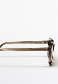 Brązowe okulary z acetatu z czarnymi akcentami, o eleganckim, prostokątnym kształcie i metalowych zawiasach. Zauszniki są smukłe z subtelnym logo.