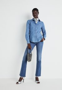 Koszula dżinsowa, z długimi rękawami, zapinana na guziki, jasnoniebieski kolor. W zestawie z niebieskimi dzwonami i srebrnymi sandałami na wysokim obcasie. Mała torebka w wzorki.