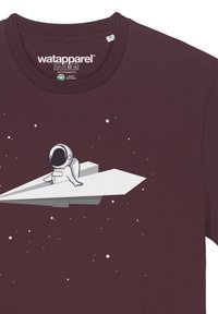 Bordeaux T-shirt met een witte cartoon astronaut op een papieren vliegtuig, omringd door kleine witte sterren. Gemaakt van organisch katoen, met een ronde hals.