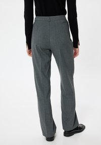 Pantalones grises ajustados con un diseño de pierna recta, un acabado texturizado y una cinturilla. Zapatos negros parcialmente visibles en el dobladillo.