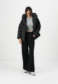 Čierna prešívaná bunda s kapucňou, doplnená o šedý crop top a čierne široké nohavice. Biele členkové čižmy.