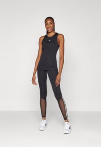 Top sportiv negru cu guler rotund, asortat cu colanți negri cu panouri transparente și dungi albe pe laterale. Sneakers albi completează ansamblul.