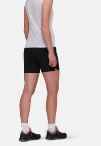 Black athletic shorts paired with a white sleeveless top. The model wears black shoes with orange accents and white socks.