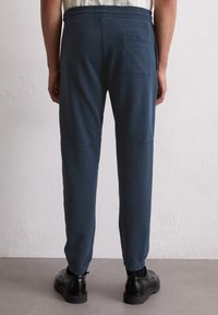 Marineblaue, schmal zulaufende Sweatpants mit elastischem Bund und einer Gesäßtasche, aus weichem Stoff mit glatter Textur und minimalen Nähdetails.