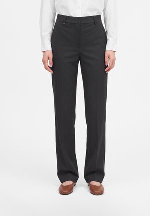 Personne portant un pantalon droit gris foncé, une chemise blanche boutonnée et des chaussures plates marron, debout les mains détendues le long du corps.