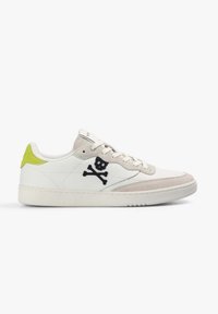 Zapatilla baja blanca con acentos beige, lengüeta trasera de neón amarillo y logo de calavera y huesos cruzados en negro en el lateral.