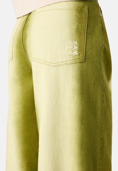 Pantalones de pana verde con una textura en degradado, que cuentan con un bolsillo trasero con logo bordado y detalles de costura visibles.