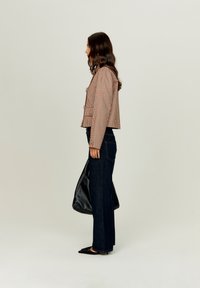 Kurtka w kratę, krótka, w kolorze brązowym i białym, połączona z ciemnoniebieskimi spodniami o szerokich nogawkach; modelka trzyma czarną torbę na ramię, stojąc z boku.