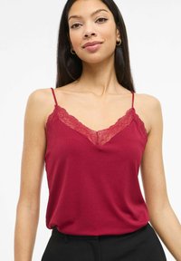 Burgundowa kamizelka z koronkową lamówką na dekolcie i cienkimi ramiączkami, wykonana z gładkiej tkaniny, o luźnym kroju.