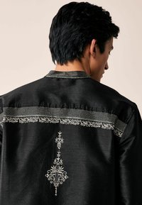 Black satin shirt featuring intricate white embroidery along the yoke and back, with a central decorative pattern. Textured and smooth finish.
