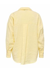 Chemise jaune surdimensionnée, en tissu texturé, avec col classique, manches longues avec poignets boutonnés, et un empiècement au dos.