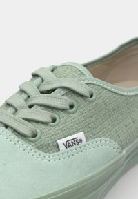 Zapatillas de lona verde claro con detalles texturizados, seis cordones a juego, costuras blancas y una pequeña etiqueta con el logo de Vans en el lateral.
