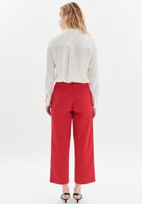 Vit blus med krage och långa ärmar, kombinerad med högmidjade röda vida byxor och svarta klacksandaler. Enkel och figurnära design.