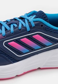 Zapatilla deportiva azul hecha de malla y material sintético. Presenta franjas en degradado rosa y púrpura, suela blanca gruesa y detalles texturizados.