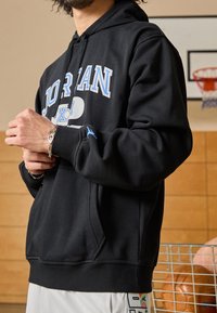 Felpa nera con testo blu "JORDAN" e logo, presenta una tasca a marsupio e polsini a costine. Tessuto morbido, vestibilità rilassata, progettata per il comfort.