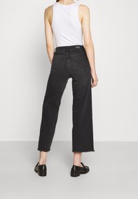 Černé široké džínové kalhoty s třepeným lemem, vysokým pasem a zadními kapsami. Kombinované s bílým tílkem a černými botami.