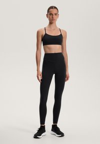 Musta urheiluasu, johon kuuluu tiukka urheiluliivi ohuiden hihnojen kanssa ja korkea vyötärö legginsit. Sileä kangas matalla pinnalla, yhdistettynä mustiin lenkkarit.