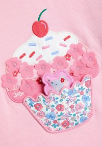 Ružová látka s designom cupcakes obsahuje bielu polevu, červenú čerešňu, ružové kvety a modrý obal so kvetinovým vzorom. Obsahuje aj vyšívané prvky.