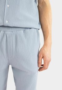 Ljusblå ribbad loungeklädsel med knäppt topp och byxor med elastisk midja. Slät textur, avslappnad passform och subtila designdetaljer.