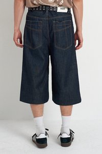 Tamni traper culotte hlače s labavim krojem, s stražnjim džepovima, kontrastnim šavovima i pojasom s logom. Uparene s bijelim čarapama i tenisicama.