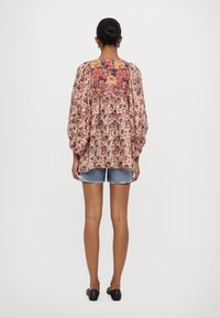 Bluse mit floralem Muster aus weichem Stoff, mit Puffärmeln und runder Halslinie, kombiniert mit Jeans-Shorts. Farben sind Pink, Rot und Blau.