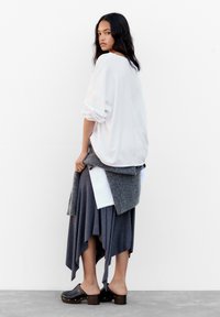 Lagenlook-Outfit mit einem weißen, oversized Oberteil, einem grauen asymmetrischen Rock und schwarzen Holzclogs mit Absatz. Weiche Texturen, lässiges Design.