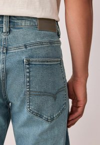 Lyseblå denimjeans har en tætsiddende form, fremtrædende baglommer med dobbeltsyning og et læderlogo på linningen.