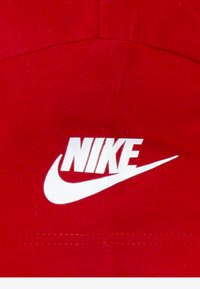 Röd keps av mjuk bomull, med en vit Nike-logotyp och swoosh-design. Sytt detaljarbete synligt längs kanten.