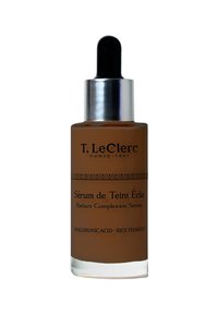 T. LeClerc Radiant Complexion Serum in einer braunen Glasflasche mit einem silbernen Tropfer, mit schwarzem Text und ornamentalen horizontalen Mustern.