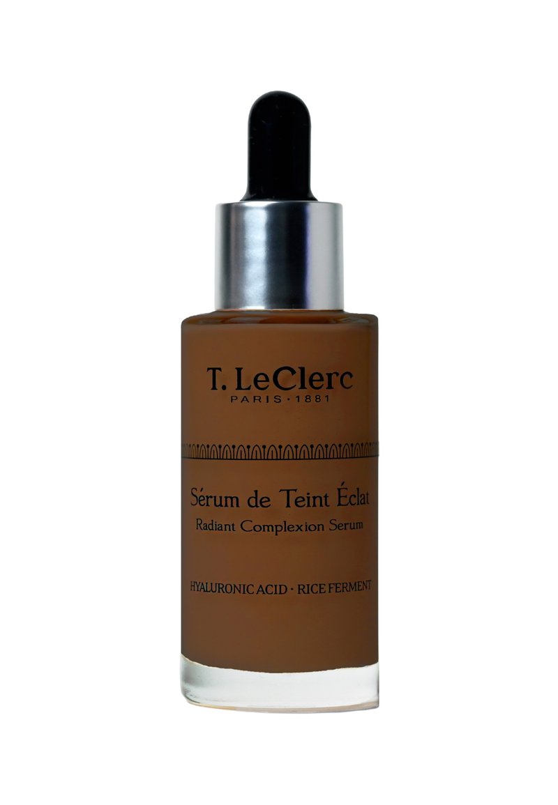 T. LeClerc Radiant Complexion Serum in einer braunen Glasflasche mit einem silbernen Tropfer, mit schwarzem Text und ornamentalen horizontalen Mustern.