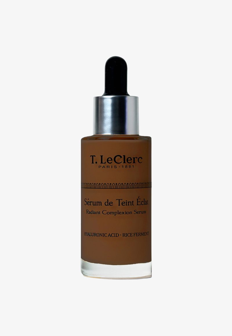 T. LeClerc Radiant Complexion Serum in einer braunen Glasflasche mit einem silbernen Tropfer, mit schwarzem Text und ornamentalen horizontalen Mustern.