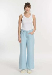 Lichtblauwe wijde jeans met een hoge taille, voorzien van twee zijzakken, gecombineerd met een witte tanktop en witte sneakers.