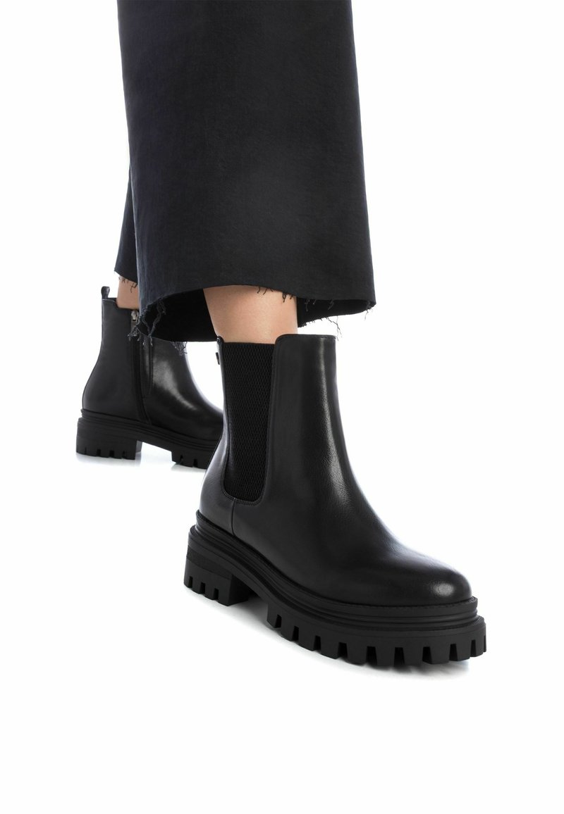 Botas de cuero negras hasta el tobillo con paneles laterales elásticos y suelas de goma gruesas, con una superficie lisa y acentos texturizados en la suela.