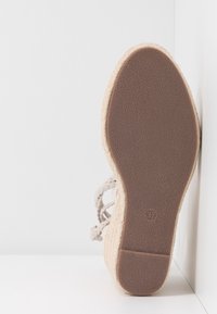 Semelle d'une sandale compensée beige avec une semelle en caoutchouc texturée et une tige en tissu tressé, affichant la taille 37 marquée sur la semelle.