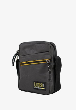 Bolso rectangular negro con superficie texturizada. Cuenta con un bolsillo amarillo con cremallera, correa de tela y una parche con el logo. Cierre superior con cremallera.