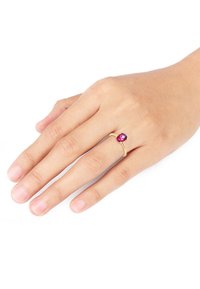 Guldring med en facetteret lyserød ædelsten sat i et enkelt bånd. Hånd med lys hud under, fingre let spredt.